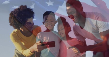 Standing family of four wearing T-shirts sharing smartphone outdoors, with American flag overlay