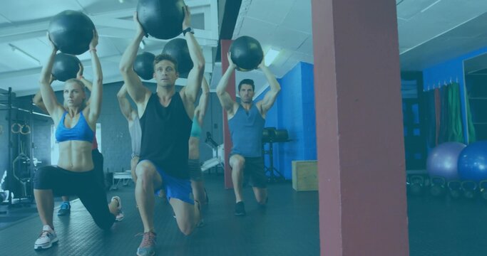 Fototapeta Five classmates performing synchronized lunges in gym with black medicine balls and kettlebells