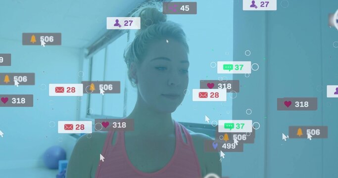 Standing trainer wearing pink tank top at studio, with exercise ball and notification icons