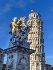 The Carrara marble fountain of the Putti, located at the entrance to the Piazza dei Miracoli, frames the Leaning Tower of Pisa, Italy