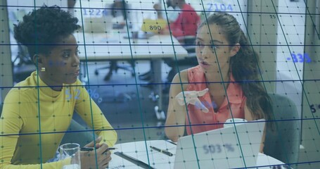 Two women in yellow top and coral blouse collaborating in office meeting, with laptop and partition