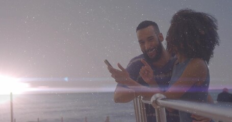 Leaning couple viewing smartphone on metal railing overlooking ocean horizon at sunset, copy space