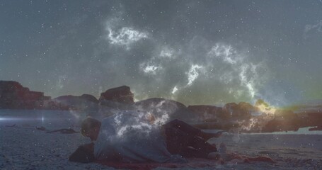 Hugging couple lying close together on sandy beach shore at dusk, with small blanket