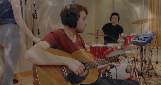 Strumming guitarist in red tee and headphones in studio, with acoustic guitar and drum kit - Powered by Adobe