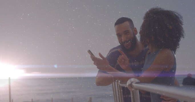 Leaning couple viewing smartphone on metal railing overlooking ocean horizon at sunset, copy space