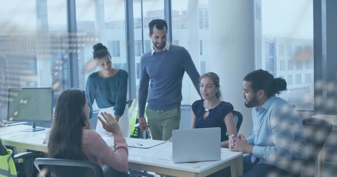 Team examining printed documents using laptop at conference table near windows with monitor, chairs