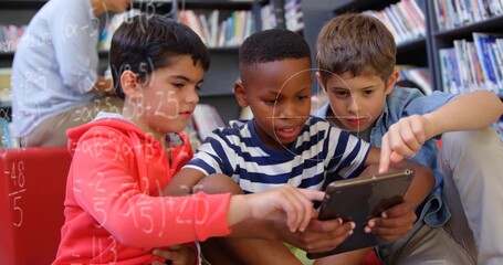 Sitting three boys pointing at tablet on red bench in library area, surrounded by bookshelves