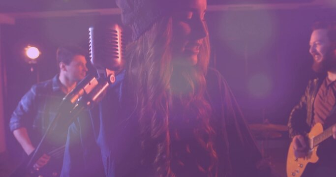 Singing vocalist wearing beanie leaning into microphone on stage, with bass and guitar, purple haze - Powered by Adobe