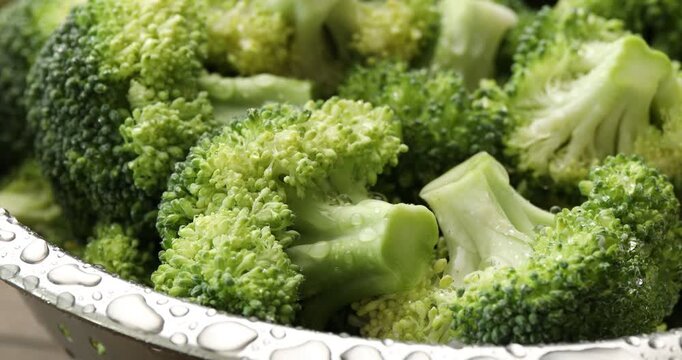Spraying water onto fresh green broccoli in colander at table, closeup