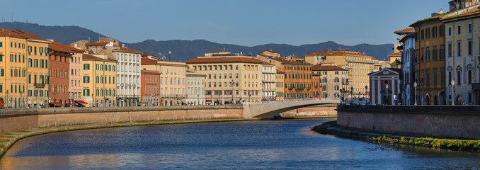 View of the Arno River with the Ponte di Mezzo bridge and pastel-colored buildings in the historic...