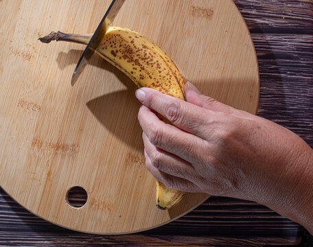 Manipulacion de alimentos, manejo de comida en la cocina, manos cortando platano con un cuchillo sobre una tabla de cortar 