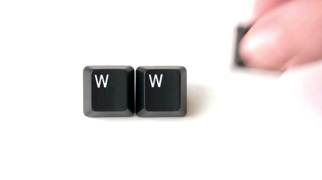 Two 'W' keyboard keys are placed side-by-side on a white surface, with a third key being held by a blurred hand in the background.