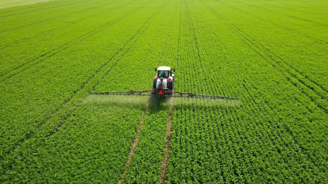 An aerial view of a tractor spraying a vast green field, illustrating modern farming and agricultural technology perfect for videos about food production, science, and crop care