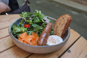 Fresh salad bowl with sausage and egg on wooden table