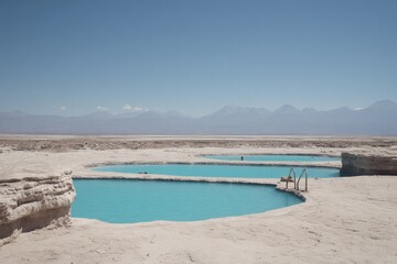Obraz premium Turquoise pools nestled in a pale desert landscape, mountains in the distance