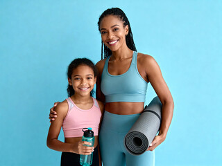 Happy Black mother and daughter in athletic wear smiling, ready for yoga or fitness with mat and water bottle against a vibrant blue studio background.