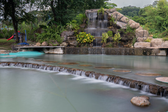 A serene landscaped waterfall surrounded by greenery at De'camp hill ka-ang, Nakhon Nayok, with a dreamy turquoise pond.