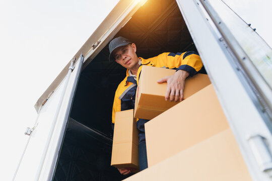 Delivery worker unloading cardboard boxes from a transport truck during sunny day at logistics warehouse
