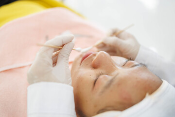 A woman is getting her eyebrows waxed by a woman in a white lab coat. The woman in the lab coat is wearing gloves
