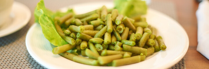 Fresh green beans served on white plate with lettuce garnish in close-up dining setting.