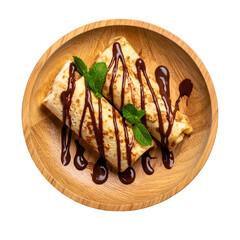 Two rolled crepes drizzled with chocolate sauce and mint, in a wooden bowl on black