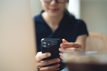 Woman using mobile phone and laptop checking email or news online while sitting at home. Searching internet social networks or remote working at coffee shop, business casual, closeup
