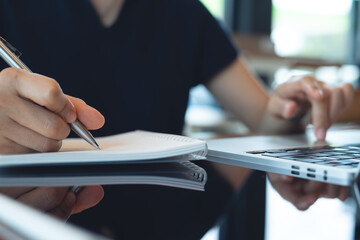 Business woman hand writing on notebook and research with laptop computer at home office. Freelancer online research, remote work and meeting agenda, business planning. Student studying online