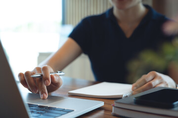 Business woman working on laptop computer, hand writing on notebook, online research at coffee shop. Freelancer remote working and meeting agenda, business planning. Student studying online, closeup