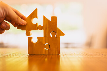 Hand assembling wooden house puzzle pieces symbolizes home building, real estate investment,...