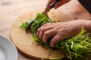 Manipulacion de alimentos, manejo de comida en la cocina, manos cortando manojo o ramas de cilantro sobre una tabla de cortar de madera