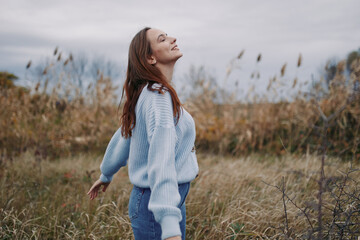 Young woman breathes deeply in a windswept field, a candid natural pose conveying genuine, authentic emotion and a trustworthy connection with nature and self under soft overcast light.