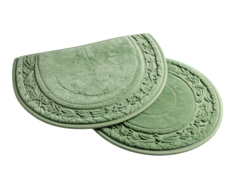 Two sage green, semi-circle bath mats with floral trim, isolated on black