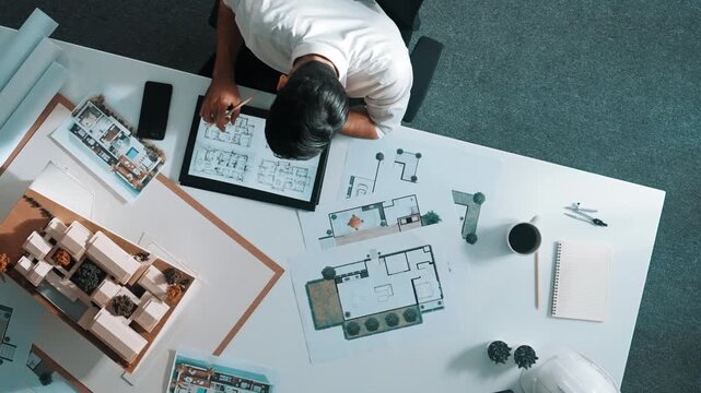 Top view of business man using tablet plan house design while sitting at meeting table with blueprint and equipment scatter around. Aerial view of civil engineer working at blueprint. Alimentation.