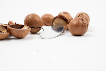 Group of whole and cracked macadamia nuts on white background, with exposed kernels inside broken shells.