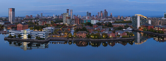 Blue hour aerial view over Salford Quays with building lights and reflections on calm evening water.
