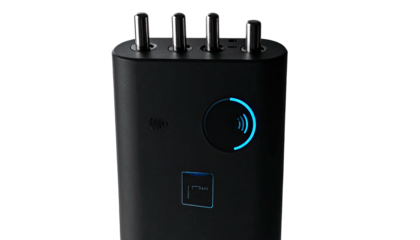 Black electronic device with 4 metal posts, glowing blue ring, and square button