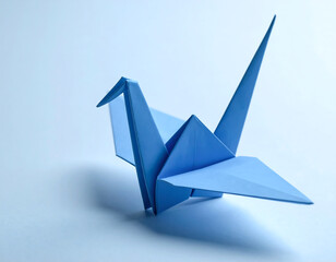 A single blue origami crane stands on a white surface, casting a soft shadow.