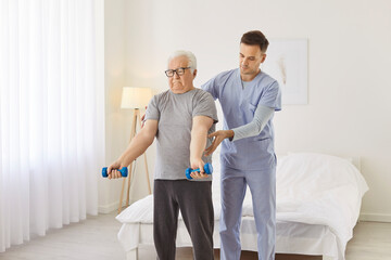 Fototapeta premium Health care worker helping senior elderly man to do exercises with dumbbells in nursing home. Physiotherapist helping retired person in rehab in rehabilitation center. Sport in retirement concept.