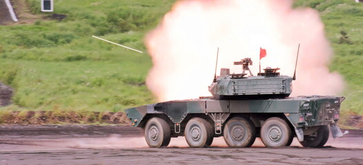 The robust eight wheeled vehicle generates a dramatic muzzle flash during a live fire exercise at the outdoor range, showcasing its formidable firepower in a dynamic moment.