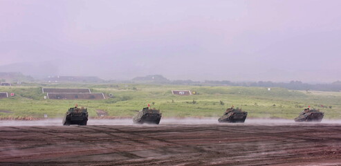 Armored vehicles engage targets on a vast military range, demonstrating intense combat readiness...