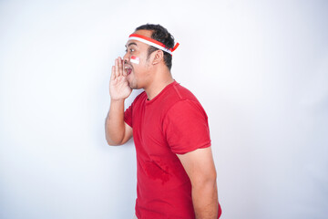 Indonesian men celebrate Indonesian independence day wearing a red shirt shouting and screaming loud with a hand on his mouth. white background.