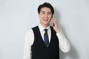 スマホで通話をするベストを着た日本人男性