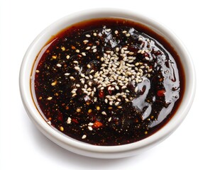 Close-up of a dark, glossy sauce in a small white bowl. Toppings include sesame seeds and possible chili flakes