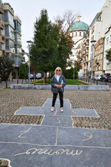 Elderly woman standing on a hopscotch game drawn with chalk on cobblestone pavement in a city street. Urban nostalgia and playful spirit meet in this cheerful moment of childhood memories and outdoor 