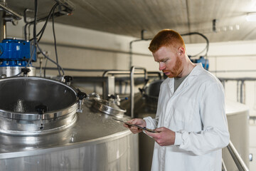 Man in lab coat monitoring fermentation process within a modern brewery using digital tablet for quality control