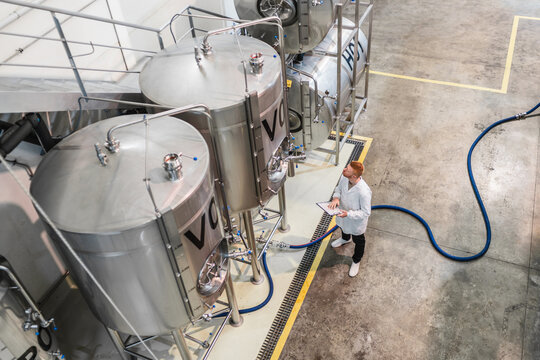 Worker checking production process and quality control data in a modern industrial beer brewing factory