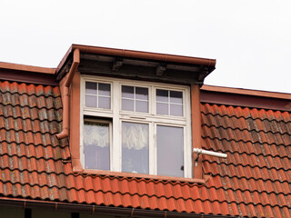 A large, rectangular dormer window with a white frame and multiple panes set into a red tiled roof against a plain sky.