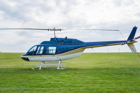 bell 206 helicopter blue white parked green grass field small aircraft skid landing gear cloudy sky outdoor aviation concept of travel, transportation, tourism