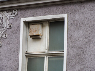 Close-up of a small window with peeling paint and an air conditioning unit on a textured purple-grey wall