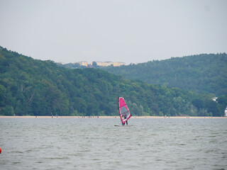 Focused shot of a windsurfer with a magenta sail sailing on the water near the lush green coastline on a cloudy day.